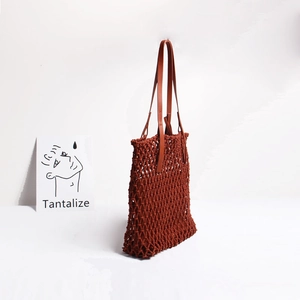 Detail of red-brown woven net bag featuring mesh texture and dark leather shoulder strap