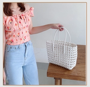 Detail of white woven tote bag with intricate cross-knit pattern and round handles