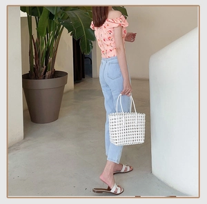 Detailed view of a white woven beach bag paired with a peach print top and jeans