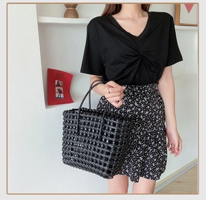Detail of hand-woven black tote bag featuring delicate grid pattern and dual handles