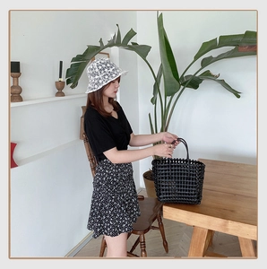 Detail of a black woven mesh tote bag with a white lace bucket hat in a cozy indoor setting