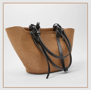 Macro detail of handwoven brown straw tote featuring black leather handles and contrast stitching