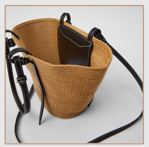Detail view of woven straw basket bag featuring black leather trim and white contrast stitching