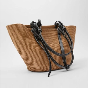 Handmade woven straw tote bag with black leather knot handles for beach vacation and travel