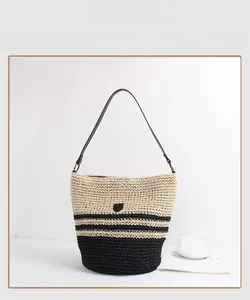 Close-up of the woven texture and leather logo on a striped straw bucket tote bag