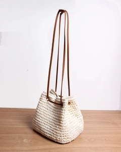 Detailed close-up of a woven straw bucket bag with elegant brown leather shoulder straps