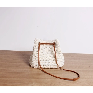 Detailed view of white hand-woven bucket bag featuring hollow pattern and brown leather strap