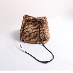 Detail view of woven straw bucket bag with drawstring closure and slim leather strap