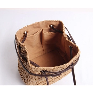 Minimalist straw shoulder bag with woven texture and brown drawstring closure for beach