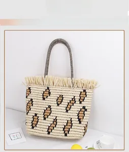 Detail of straw woven tote with leopard pattern, fringe trim, and striped round handle