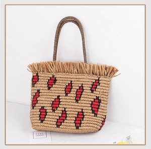 Detail of bohemian straw tote bag featuring tassel fringe and red geometric embroidery