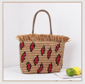 Detail of straw woven tote bag featuring red and black geometric patterns and raffia fringe