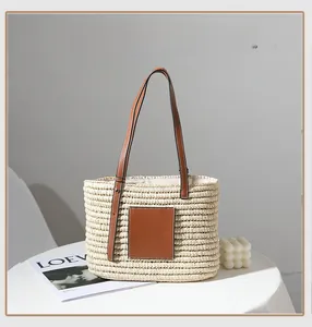 Detail of hand-woven straw tote bag featuring brown leather handles and square patch