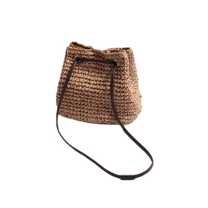 Straw bucket bag with dark brown shoulder strap and drawstring closure for beach vacation