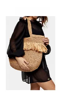 Close-up of a large straw tote bag featuring decorative tassels and woven texture