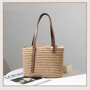 Close-up of handmade straw tote bag with brown leather handles on a white minimalist table