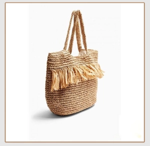 Close-up of woven straw tote bag with long tassels and wide braided shoulder straps