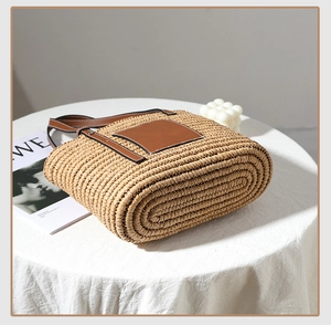Detail of hand-woven straw tote bag with brown leather straps and square patch detail