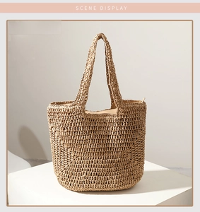 Detail of woven straw tote bag with reinforced handles and zipper closure on a white surface