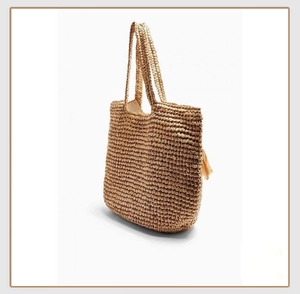 Detail view of woven straw tote bag with tassel accent and dense texture for summer