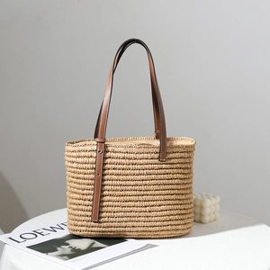 Chic square handmade straw handbag with brown leather straps on a white table