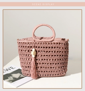 Detail of pink straw tote bag with cutout weave, round handles and tassel pendant