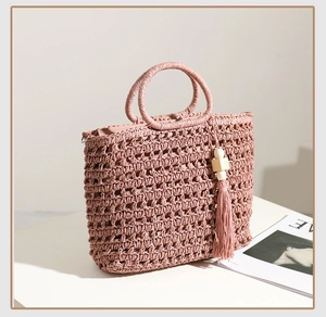 Detail of a pink straw bag with circular handles, wooden beads, and fringe tassels