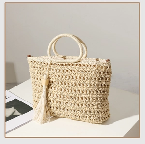 Close-up of beige woven straw tote bag with intricate cutout texture and tassel charm