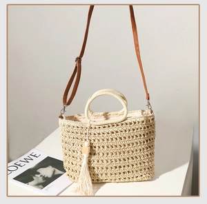Close-up of hand-woven hollow straw bag with white tassel detail and brown leather straps