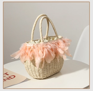 Detail of hand-woven straw bag featuring peach feather trim and rounded top handles