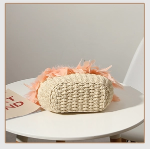 Detail of hand-woven straw bag featuring peach feathers and a sturdy oval bottom base