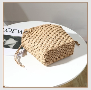 Detail of beige woven straw bucket bag with drawstring closure on a minimalist table