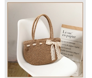 Détail d'un sac de plage tressé à la main avec un nœud en dentelle blanche et anses