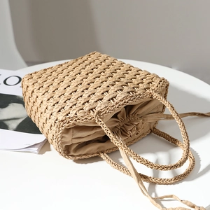 Minimalist straw woven tote bag with drawstring lining on white table for summer vacation