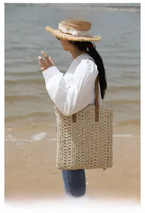 Side view of a beige woven straw tote bag with brown leather straps for beach vacations