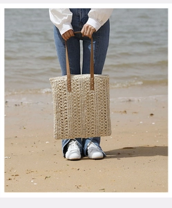Detailed texture of woven straw tote bag with brown leather handles on a sandy beach
