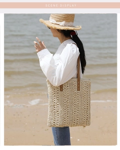 Detail of straw tote bag with brown leather strap and cross stitching at the beach