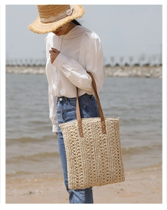 Detail of hand-woven straw tote with premium brown leather straps on a beach background