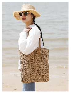 Detail of hand-woven straw tote bag with star patterns and brown leather straps on beach