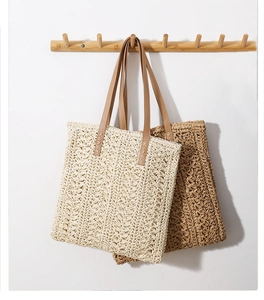 Detail of woven straw tote bag with brown leather straps hanging on a white wall