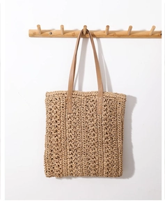 Detail of woven straw tote bag with brown leather handles and intricate floral patterns