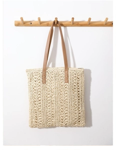 Close-up of beige crochet straw tote bag featuring brown leather handles and hollow knit patterns