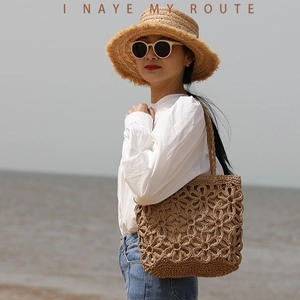 Handwoven straw tote bag with cutout floral patterns and shoulder straps for beach vacation