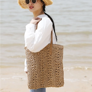 Large straw tote bag with brown leather handles on a sunny beach background