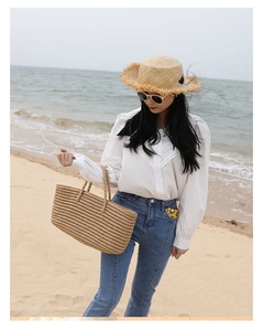 Detailed close-up of woven straw tote bag with double handles and holiday sun hat