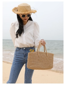 Handwoven straw tote bag for beach vacations shown in a scenic coastal outdoor setting