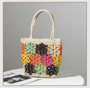 Detail einer handgefertigten Strohtasche mit bunten Häkelblumen und hohlem Webmuster-Design
