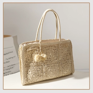 Dettaglio ravvicinato della borsa in paglia intrecciata a mano con pompon beige