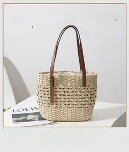 Detail of hollow straw tote bag featuring brown leather straps and drawstring liner