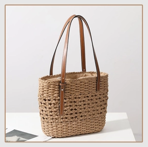 Close-up of hollow woven straw handbag with brown leather straps and silver metal rivets